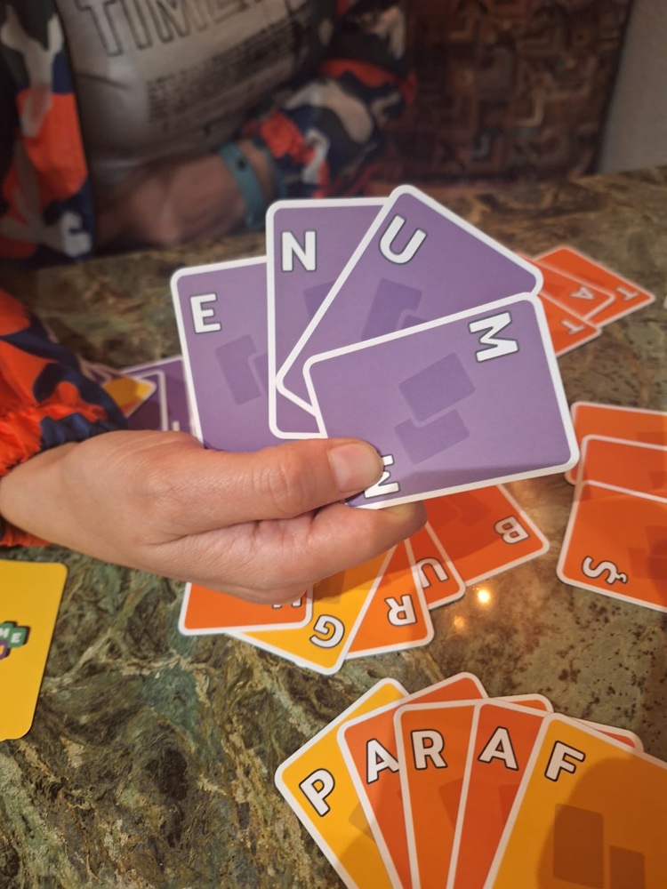 A hand of purple Kelime Kıran letter cards held over finished words on a table